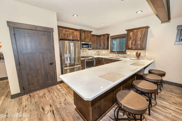 kitchen with beam ceiling, backsplash, kitchen peninsula, appliances with stainless steel finishes, and light wood-type flooring