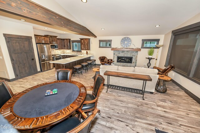 dining room featuring a fireplace, vaulted ceiling with beams, and light hardwood / wood-style flooring