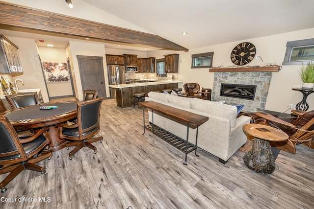 living room with a stone fireplace, lofted ceiling with beams, and light wood-type flooring