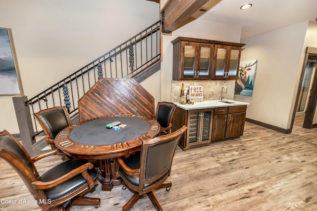 bar featuring sink, beverage cooler, backsplash, dark brown cabinets, and light wood-type flooring