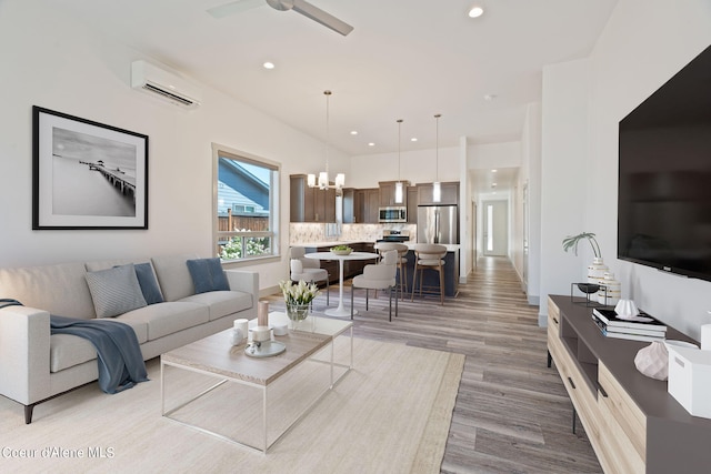 living room with light wood-type flooring, ceiling fan with notable chandelier, and a wall unit AC