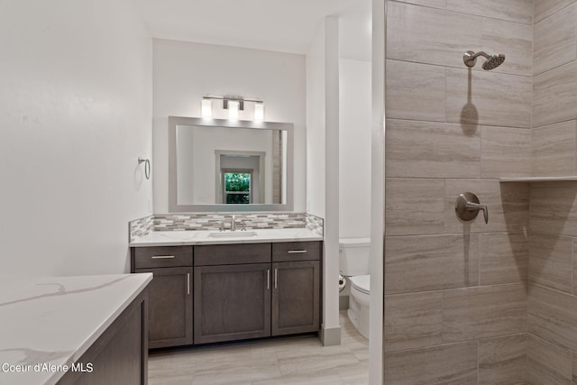 bathroom featuring vanity, toilet, a tile shower, and tasteful backsplash