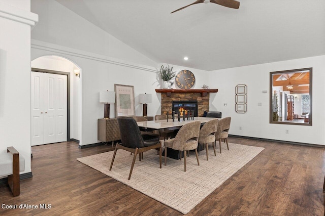 dining room with dark hardwood / wood-style flooring, ceiling fan, a stone fireplace, and high vaulted ceiling