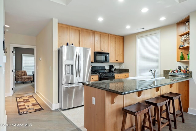 kitchen featuring kitchen peninsula, a kitchen breakfast bar, dark stone counters, sink, and black appliances