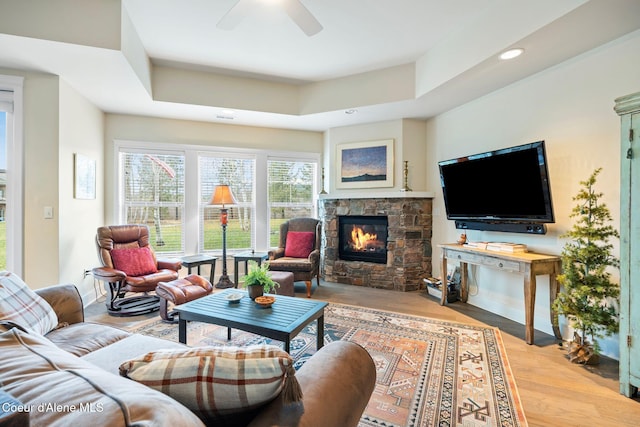 living room featuring a stone fireplace, ceiling fan, and light hardwood / wood-style flooring