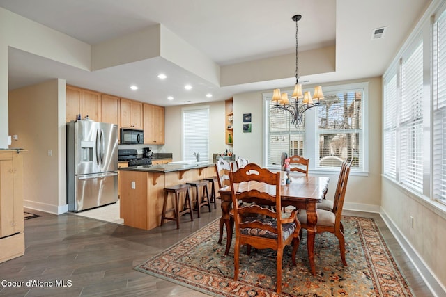 dining room featuring dark hardwood / wood-style flooring, a tray ceiling, a notable chandelier, and sink