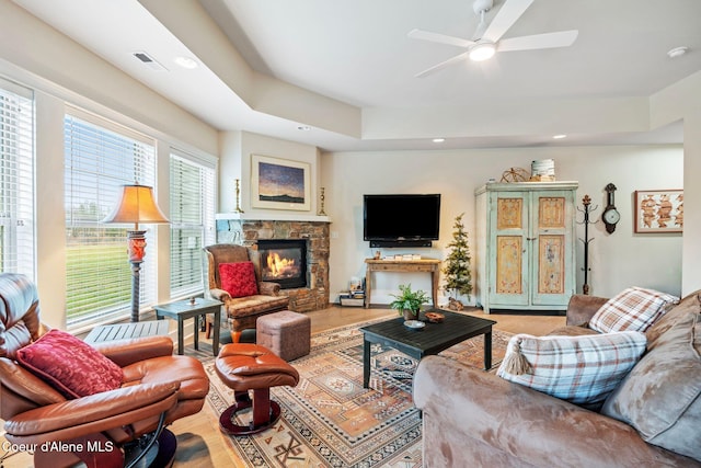 living room with a fireplace, light wood-type flooring, a tray ceiling, and ceiling fan