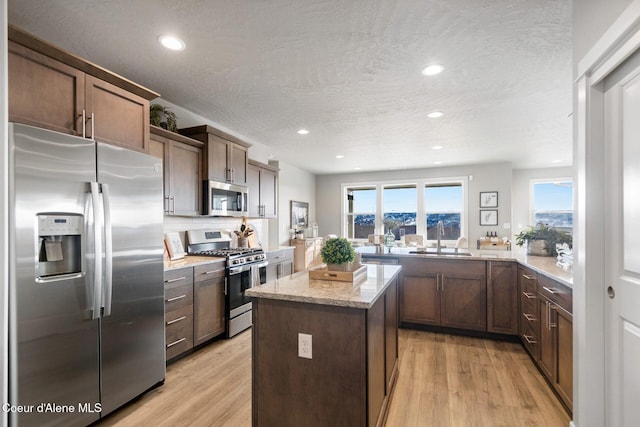 kitchen featuring appliances with stainless steel finishes, light wood-type flooring, kitchen peninsula, light stone counters, and sink