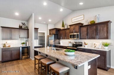 kitchen featuring wine cooler, stainless steel appliances, an island with sink, sink, and backsplash