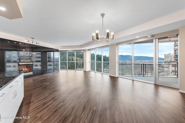 unfurnished living room featuring a mountain view, an inviting chandelier, and dark wood-type flooring