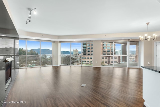 unfurnished living room featuring a mountain view, rail lighting, dark wood-type flooring, and an inviting chandelier