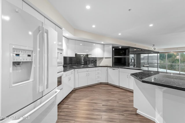 kitchen featuring sink, dark wood-type flooring, dark stone counters, white appliances, and white cabinets