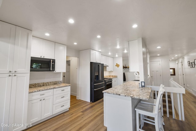 kitchen featuring high end appliances, white cabinets, a kitchen breakfast bar, light hardwood / wood-style flooring, and light stone counters