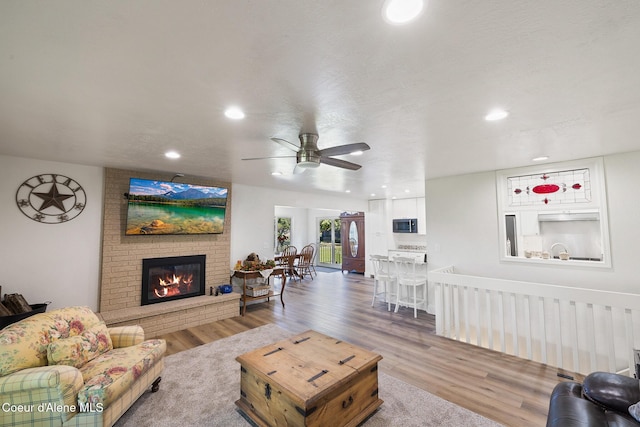 living room with ceiling fan, wood-type flooring, and a brick fireplace