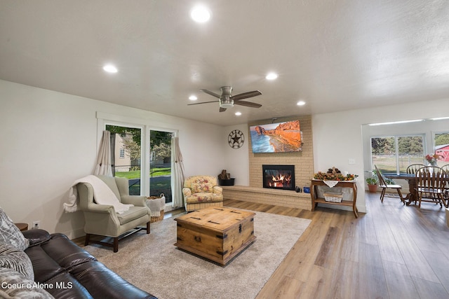 living room featuring light wood-type flooring, a brick fireplace, and ceiling fan