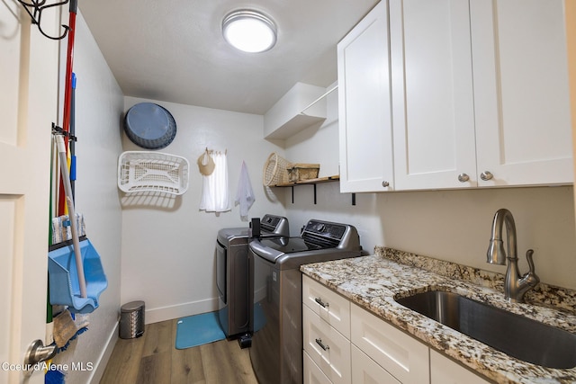 clothes washing area featuring cabinets, hardwood / wood-style floors, washing machine and dryer, and sink