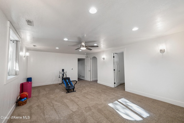 exercise area with ceiling fan, light colored carpet, and a textured ceiling