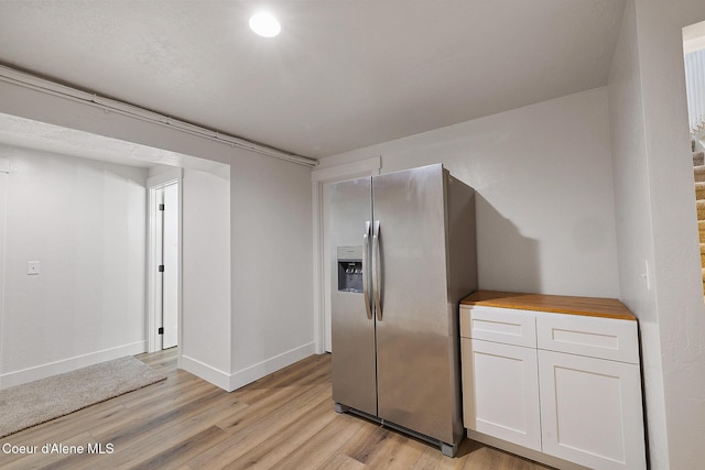 kitchen with white cabinets, stainless steel fridge, light hardwood / wood-style flooring, and wooden counters