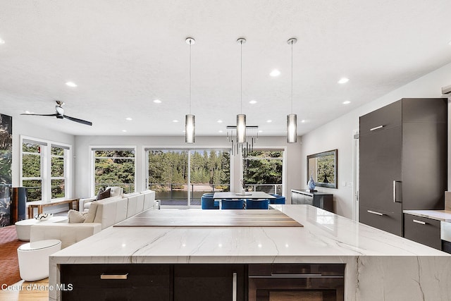 kitchen with a large island, modern cabinets, light stone counters, open floor plan, and pendant lighting