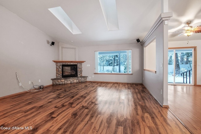 unfurnished living room featuring hardwood / wood-style floors, a stone fireplace, ceiling fan, and vaulted ceiling with skylight