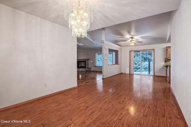 unfurnished living room featuring a stone fireplace, ceiling fan with notable chandelier, and hardwood / wood-style flooring