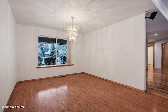 spare room featuring hardwood / wood-style flooring and an inviting chandelier