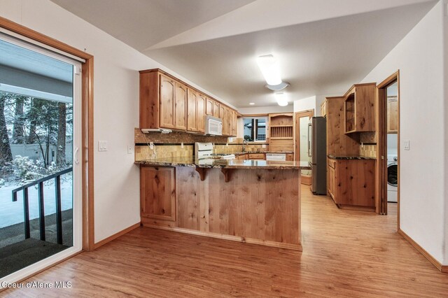 kitchen with kitchen peninsula, backsplash, white appliances, dark stone countertops, and lofted ceiling