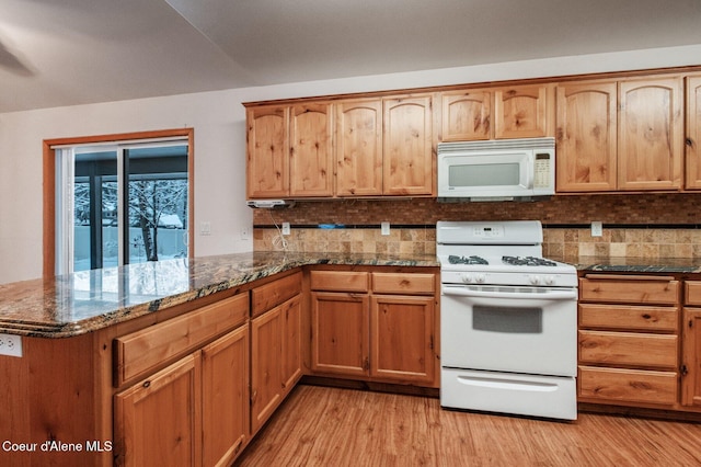 kitchen featuring white appliances, backsplash, dark stone counters, light hardwood / wood-style floors, and kitchen peninsula