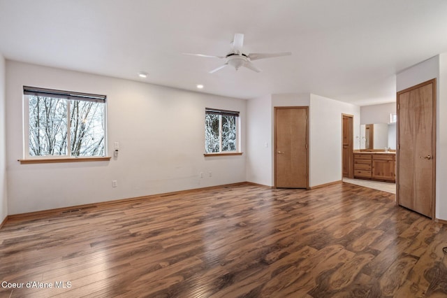 unfurnished bedroom featuring ensuite bath, ceiling fan, dark wood-type flooring, and multiple windows