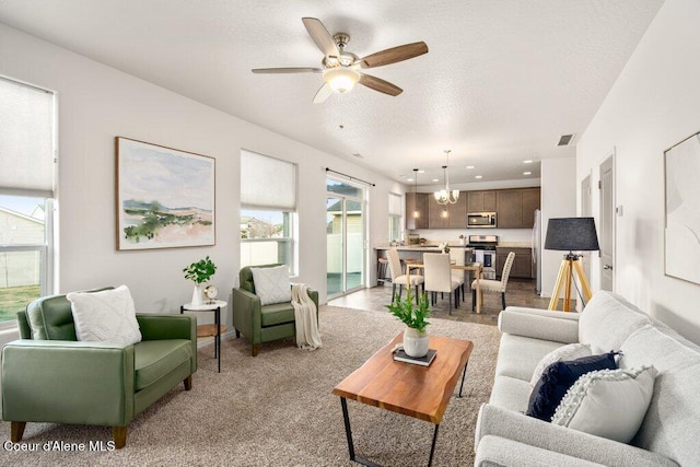 carpeted living room with ceiling fan with notable chandelier