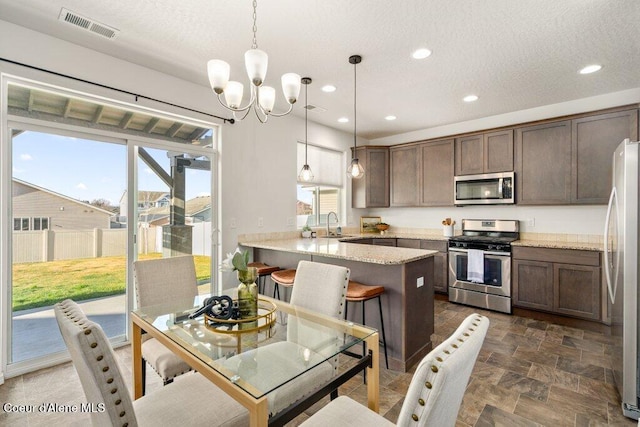 kitchen featuring light stone countertops, stainless steel appliances, kitchen peninsula, and decorative light fixtures