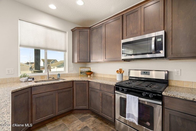 kitchen with light stone countertops, appliances with stainless steel finishes, sink, and dark brown cabinetry