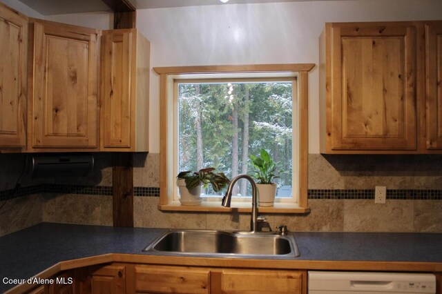 kitchen featuring backsplash, dark countertops, white dishwasher, and a sink