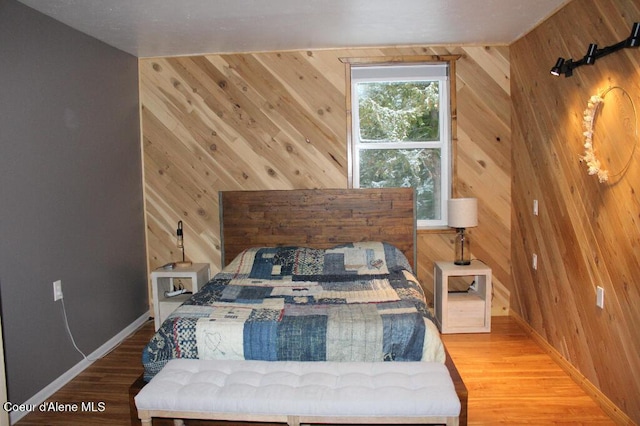 bedroom with wooden walls, wood finished floors, and baseboards