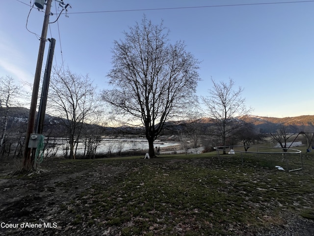 yard at dusk featuring a mountain view and a trampoline