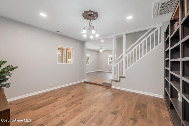 interior space with a wealth of natural light, ceiling fan with notable chandelier, and hardwood / wood-style floors