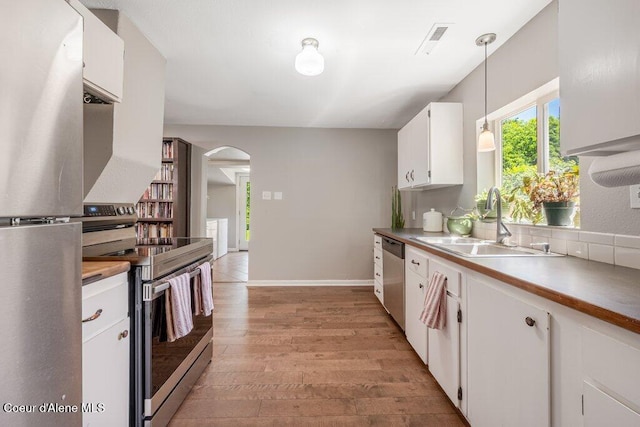 kitchen featuring sink, light hardwood / wood-style flooring, appliances with stainless steel finishes, white cabinetry, and decorative light fixtures