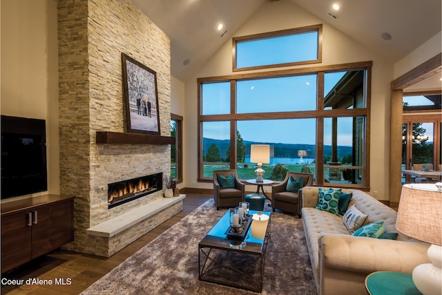 living room featuring a mountain view, high vaulted ceiling, a stone fireplace, and dark wood-type flooring