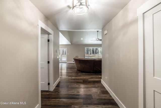 hallway with dark wood finished floors, vaulted ceiling, and baseboards