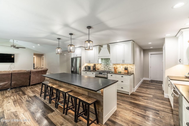 kitchen featuring stainless steel appliances, a breakfast bar area, premium range hood, dark countertops, and dark wood finished floors