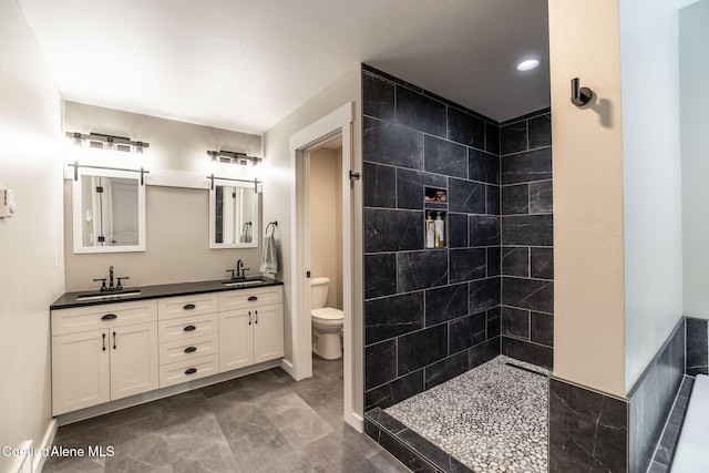 full bathroom with double vanity, a tile shower, toilet, and a sink