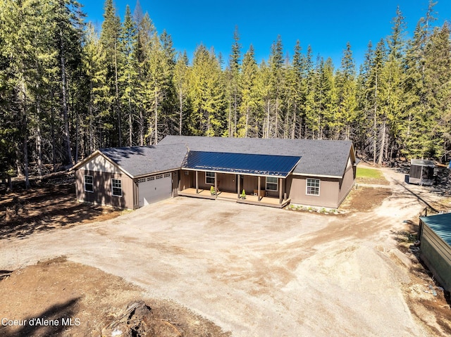 view of front of home with a porch, dirt driveway, cooling unit, a forest view, and an attached garage