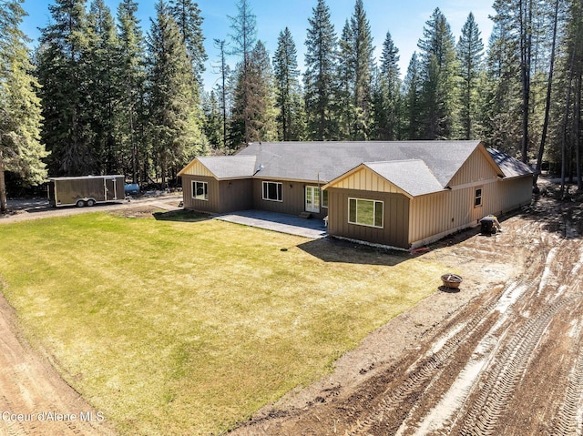 back of property with a lawn, dirt driveway, a shingled roof, and a patio area