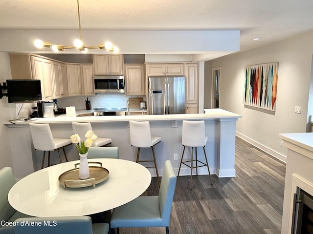 kitchen featuring a kitchen breakfast bar, light brown cabinets, hanging light fixtures, and appliances with stainless steel finishes