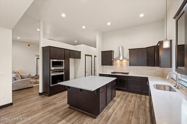 kitchen with sink, wall chimney range hood, light hardwood / wood-style floors, a kitchen island, and appliances with stainless steel finishes