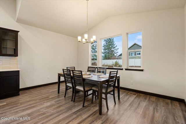 dining area featuring dark hardwood / wood-style floors, lofted ceiling, and a notable chandelier