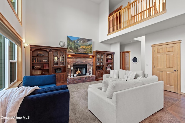 living room featuring light hardwood / wood-style flooring, a high ceiling, and a brick fireplace