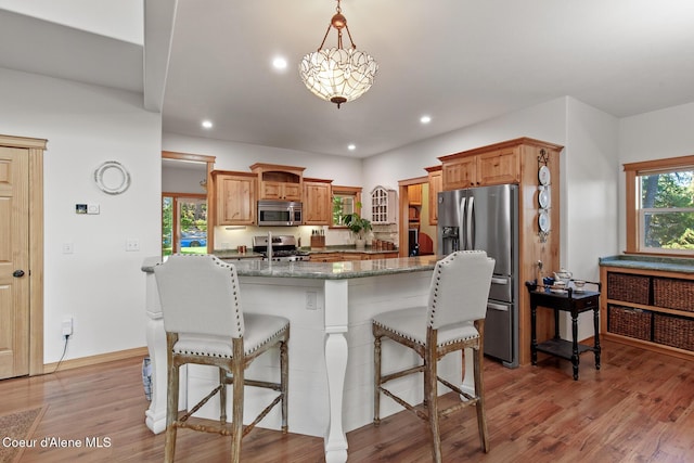 kitchen featuring stainless steel appliances, a kitchen breakfast bar, light hardwood / wood-style flooring, pendant lighting, and dark stone counters