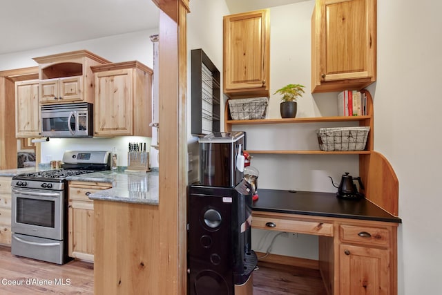 kitchen featuring appliances with stainless steel finishes, light brown cabinets, light hardwood / wood-style flooring, and dark stone counters