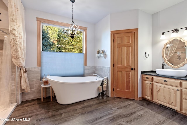 bathroom with a washtub, an inviting chandelier, wood-type flooring, vanity, and tile walls